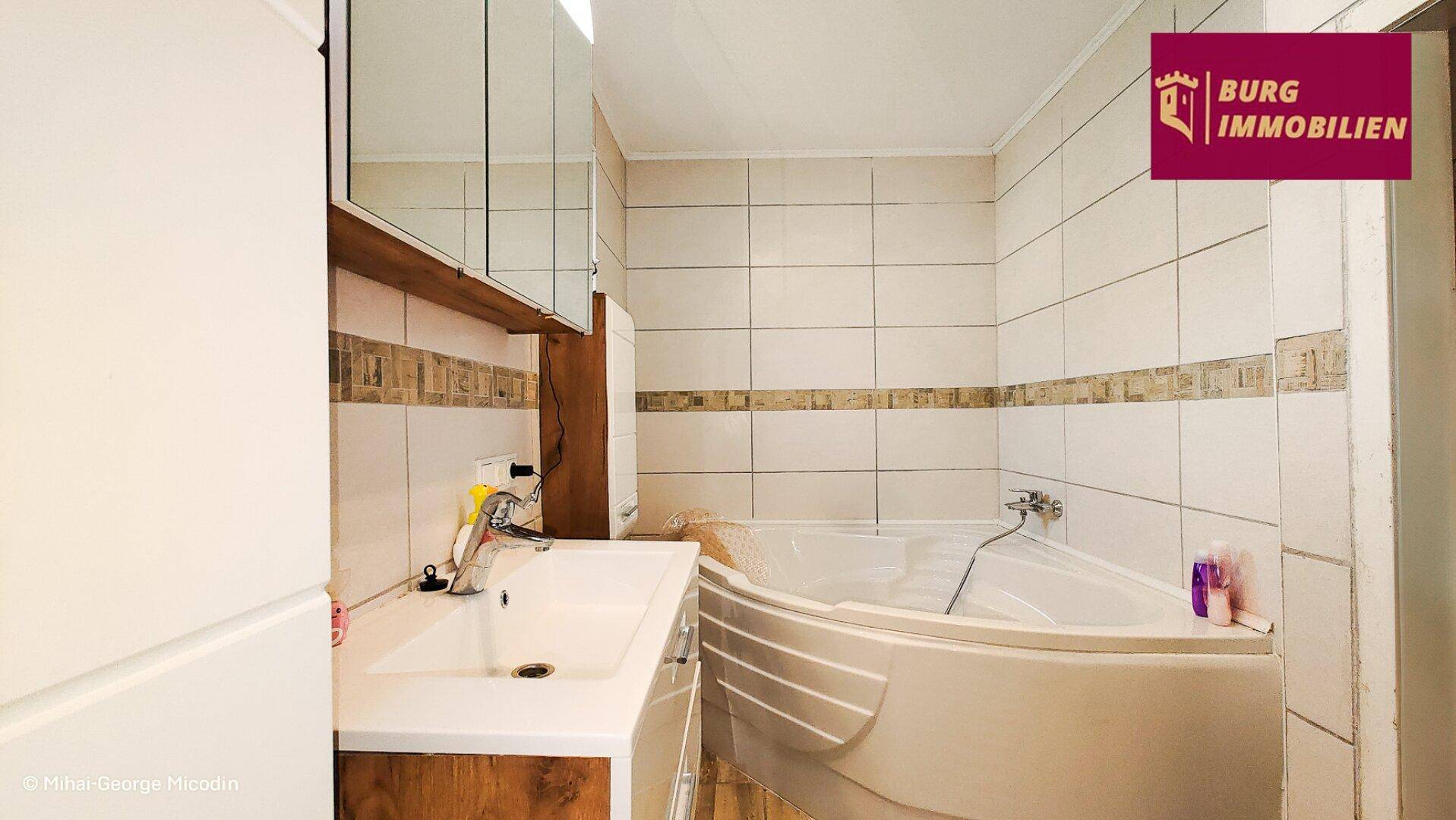 Badezimmer mit Eckbadewanne, Fliesenboden und Spiegelschrank über dem Waschbecken.