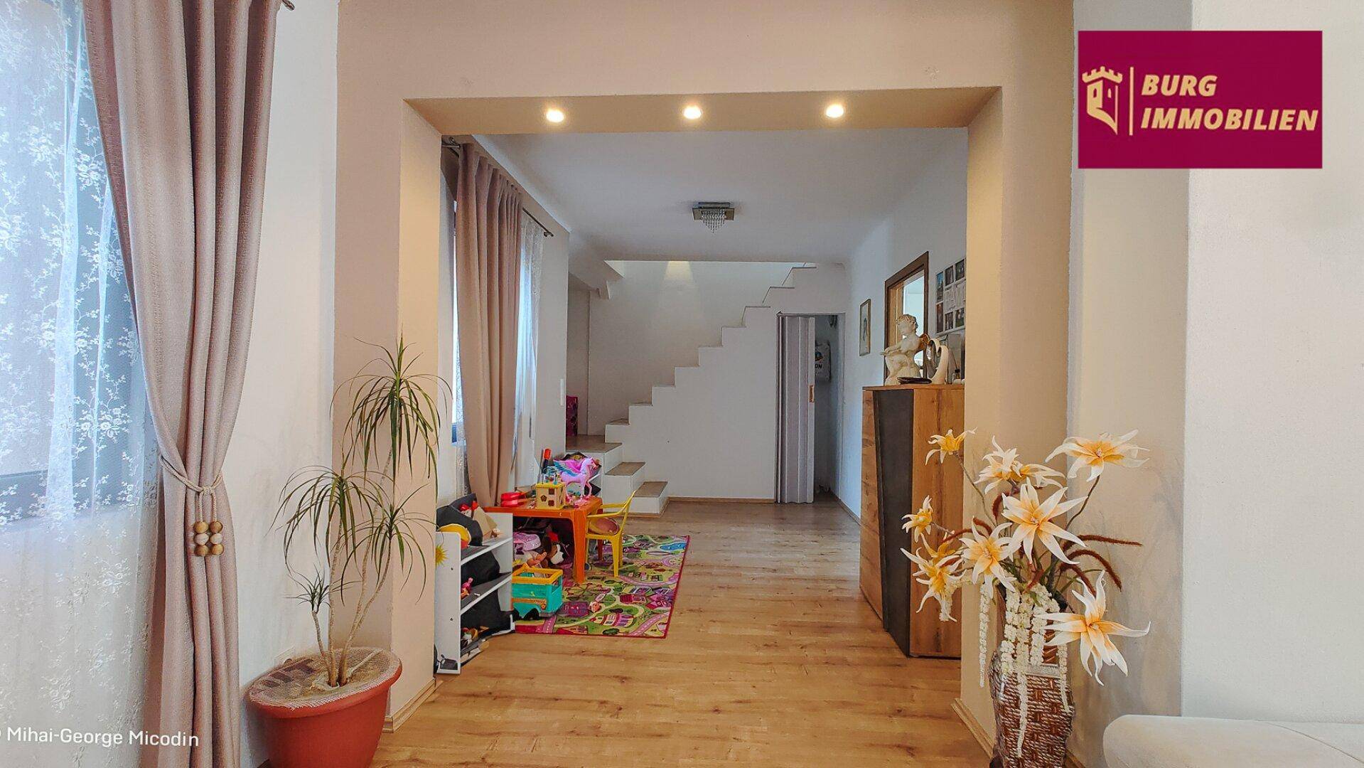 Geräumiger offener Wohnbereich mit Holzfußboden und Zugang zur Treppe ins Obergeschoss.