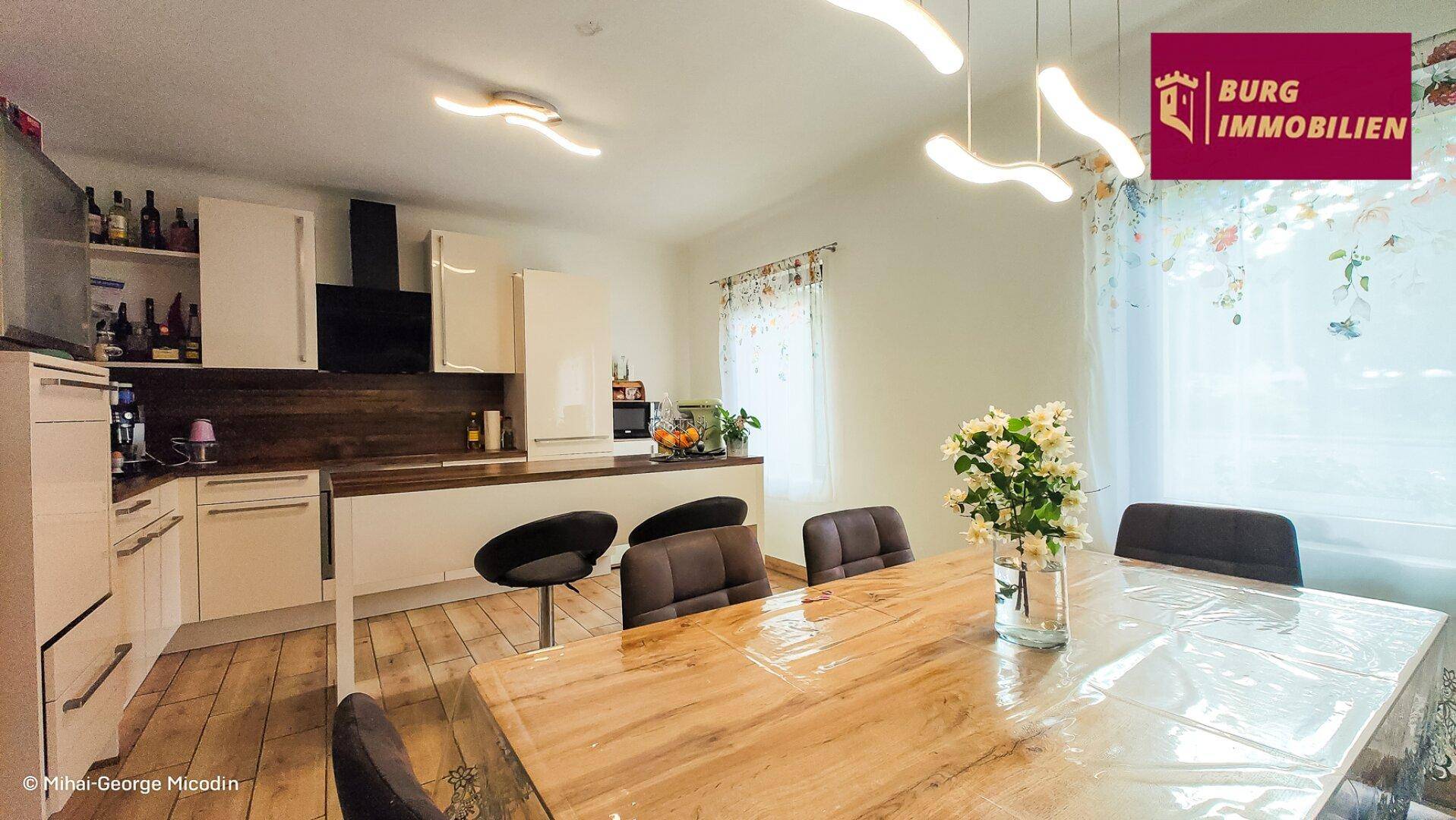 Moderne Einbauküche mit Essbereich, weißen Schränken und Holz-Arbeitsplatten.