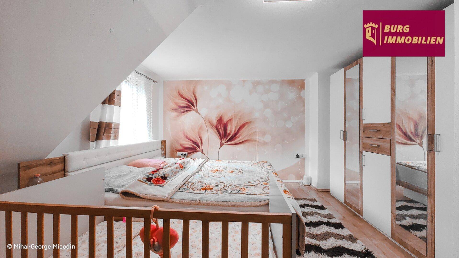 Gemütliches Schlafzimmer im Dachgeschoss mit schräger Decke und floraler Wandgestaltung.