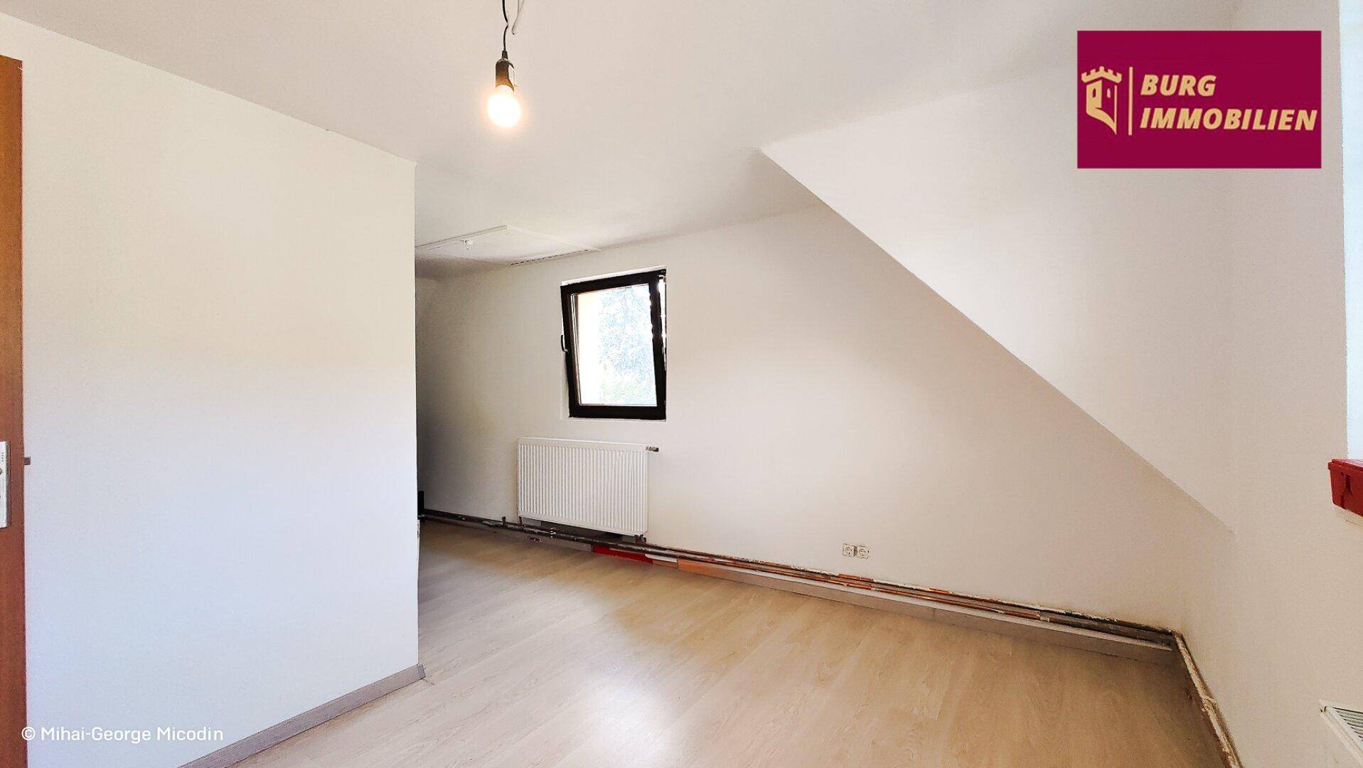 Leeres Zimmer im Dachgeschoss mit schräger Decke und einem Fenster für Tageslicht.