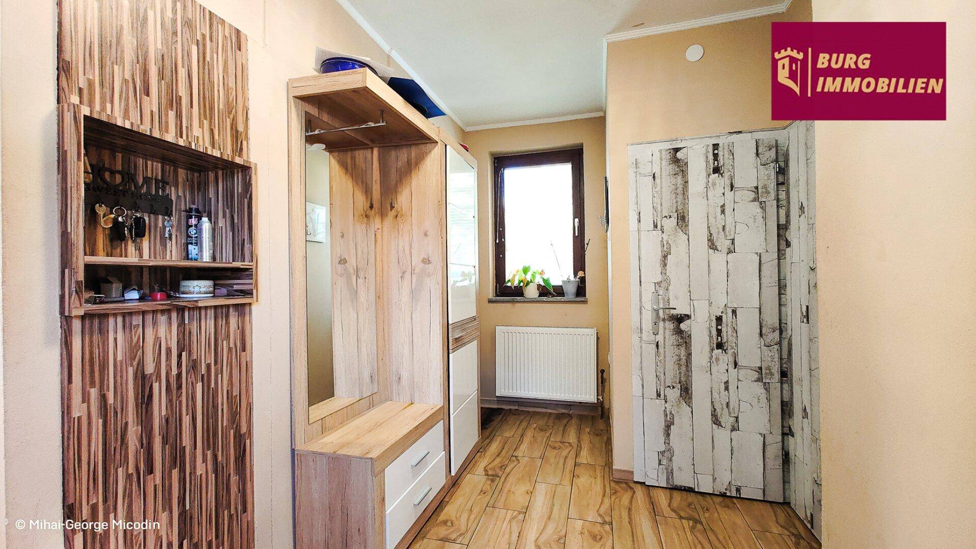 Heller Eingangsbereich mit Holzmöbeln, Garderobe und einem Fenster für natürliches Licht.