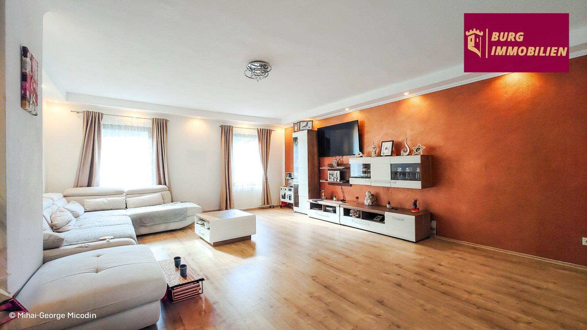 Helles Wohnzimmer mit großem Ecksofa, Medienwand und einem warmen Akzent an der Wand.