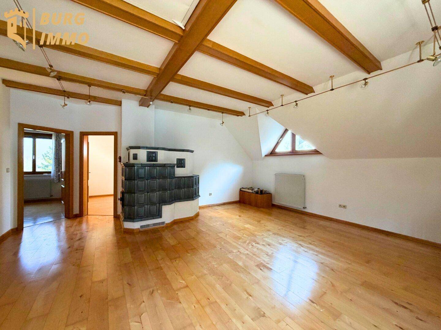 Geräumiger Wohnbereich im Dachgeschoss mit Holzbalken, Kachelofen und Holzboden.