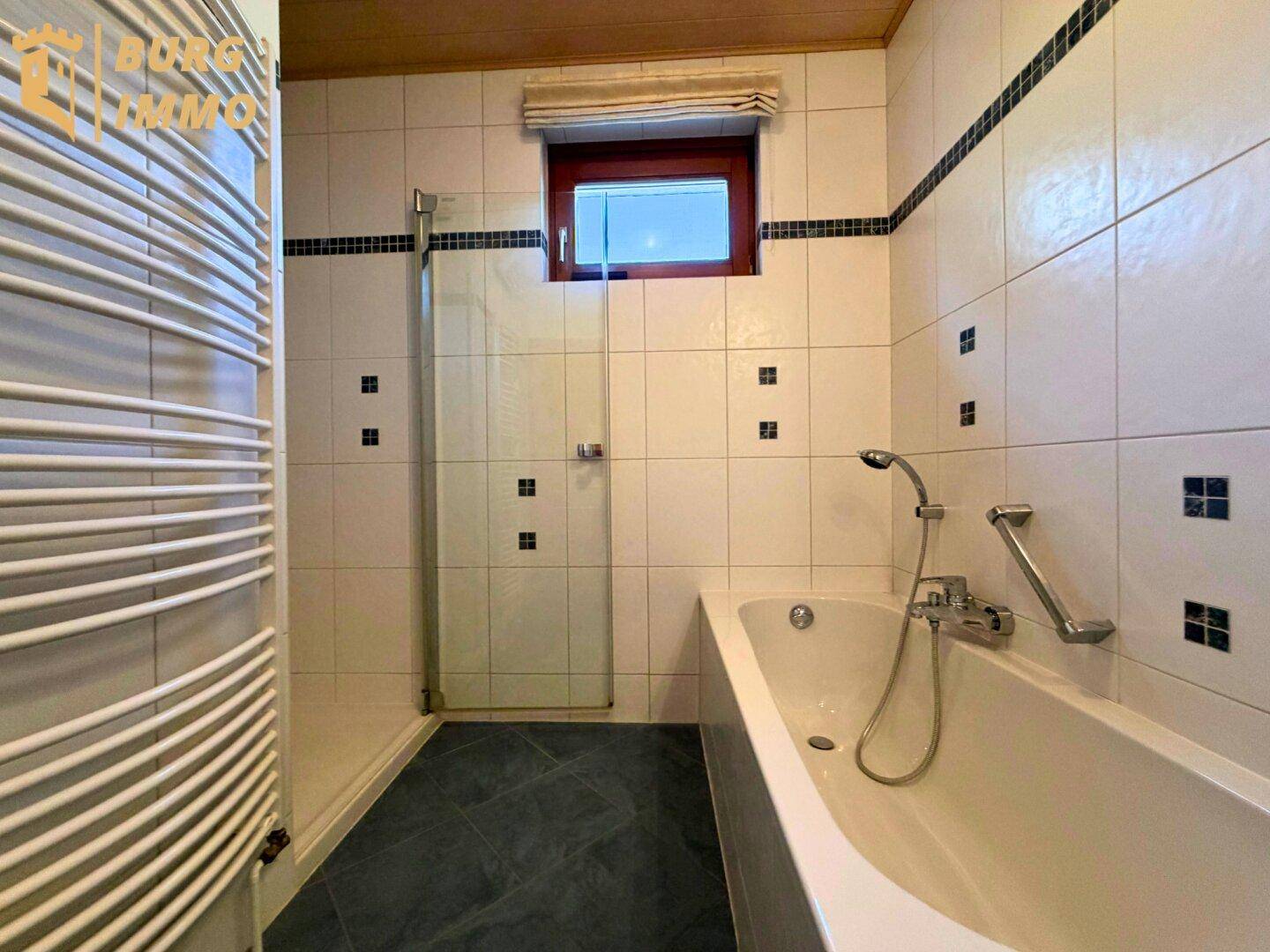 Badezimmer mit Badewanne, Duschkabine, Handtuchheizkörper und Fliesen in Weiß und Schwarz.