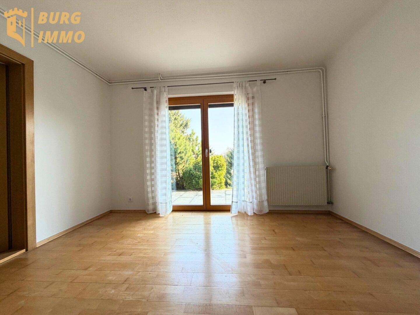 Heller Raum mit Holzboden und Zugang zu einem Außenbereich durch eine große Glastür.