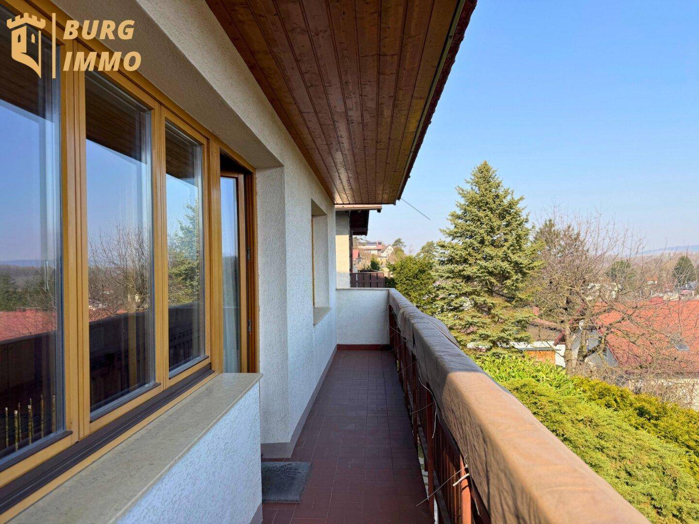 Langer Balkon mit Holzdach und Blick ins Grüne, zugänglich von den Innenräumen.