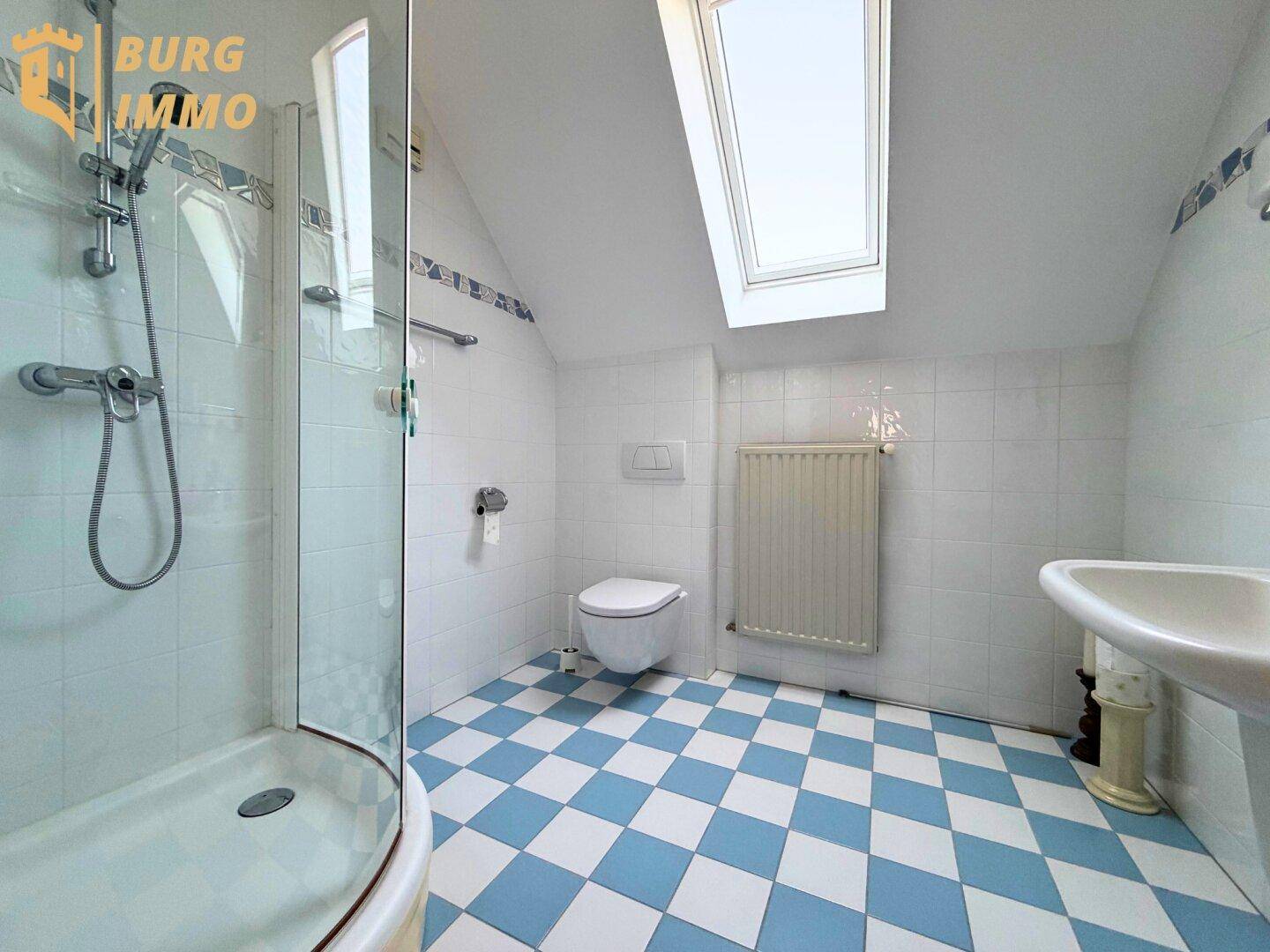 Badezimmer im Dachgeschoss mit Duschkabine, WC, Waschbecken und blau-weiß kariertem Fliesenboden.