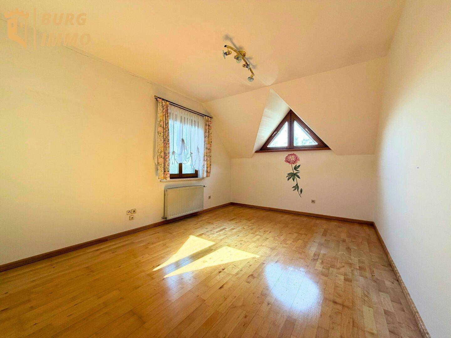 Helles Schlafzimmer mit Holzboden, Dachschräge und einem dreieckigen Fenster.