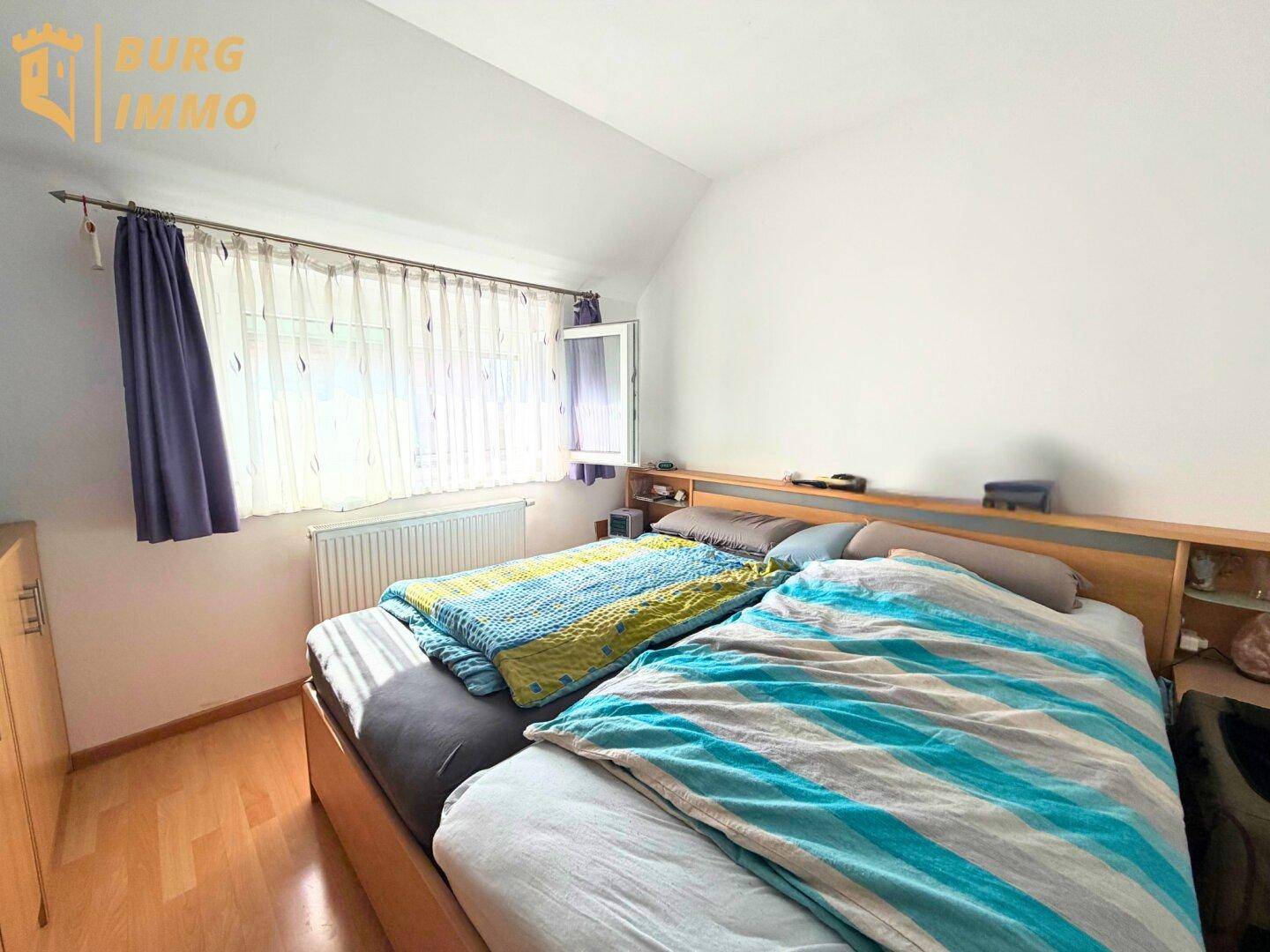 Helles Schlafzimmer mit Holzbett, Parkettboden und Fenster für viel Tageslicht.