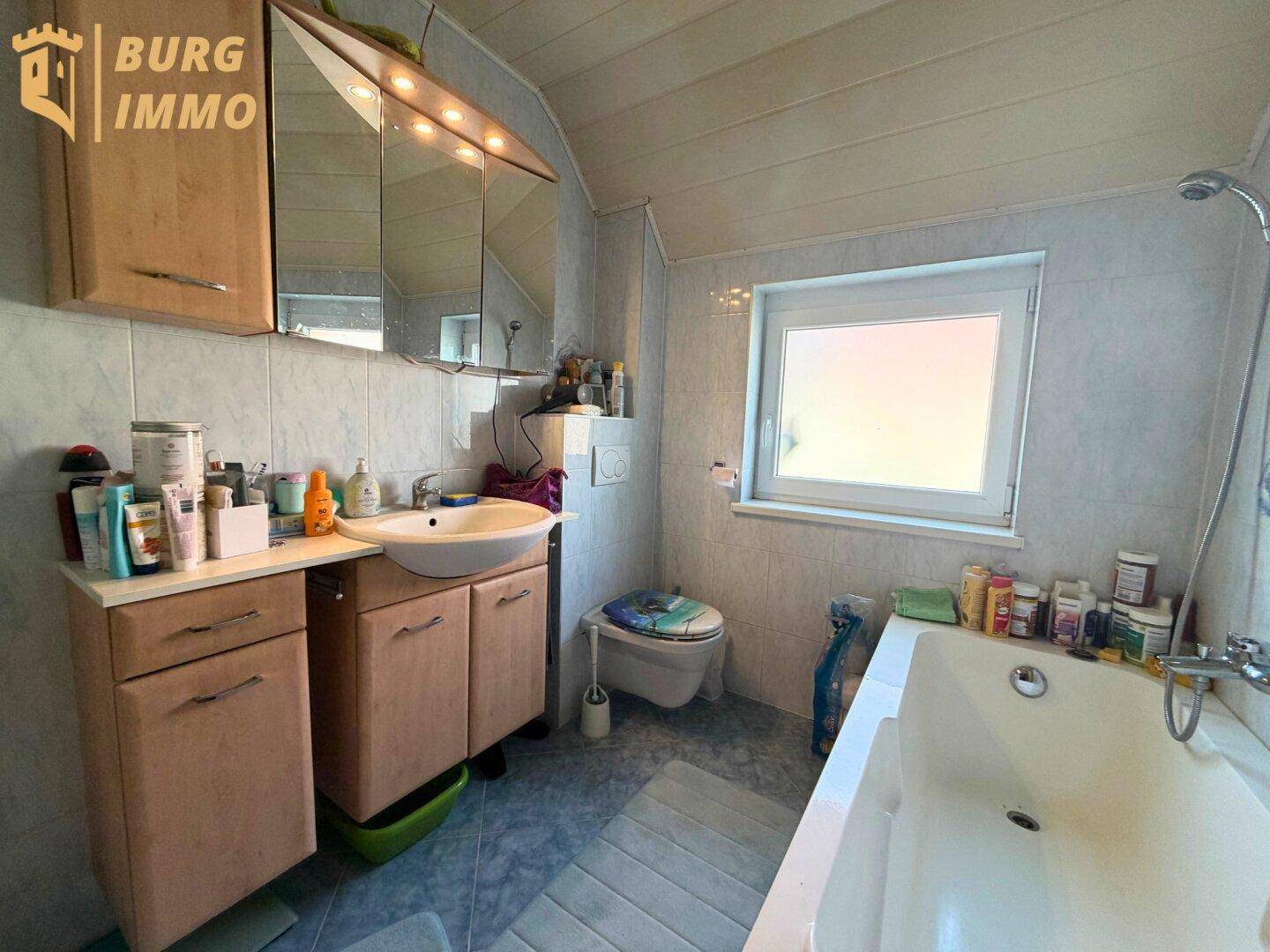 Funktionales Badezimmer mit Badewanne, Waschbecken und Fenster für natürliche Belüftung.