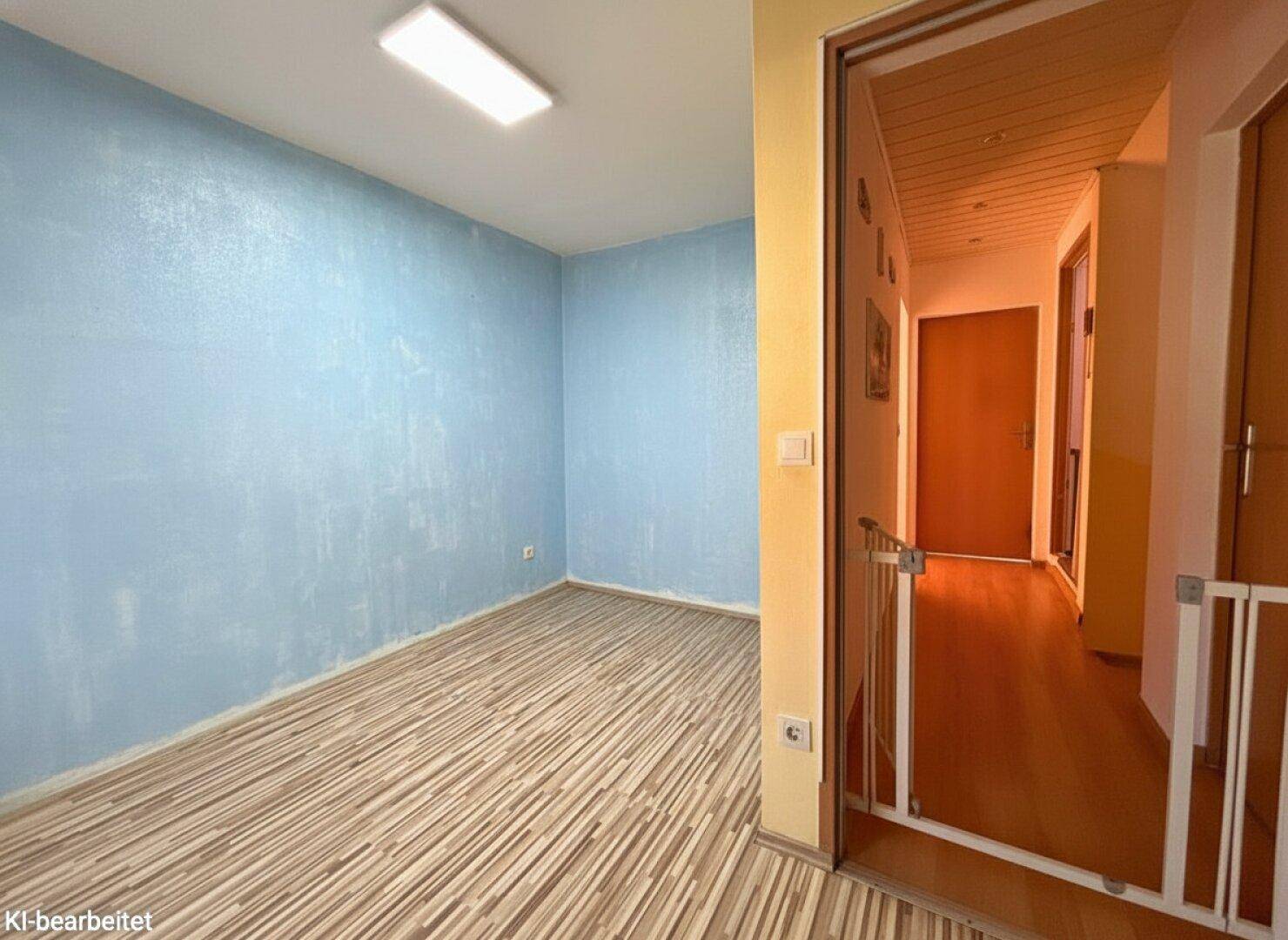 Heller Raum mit Laminatboden und Zugang zu einem Flur mit Kindersicherung.