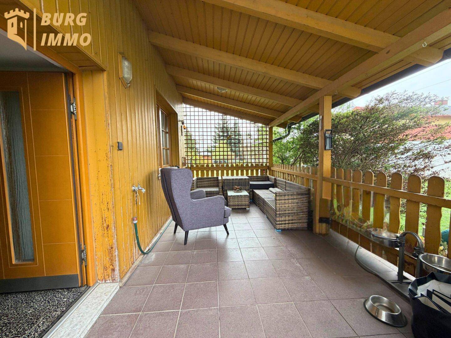 Überdachte Terrasse mit Holzverkleidung, Fliesenboden und gemütlicher Sitzecke.