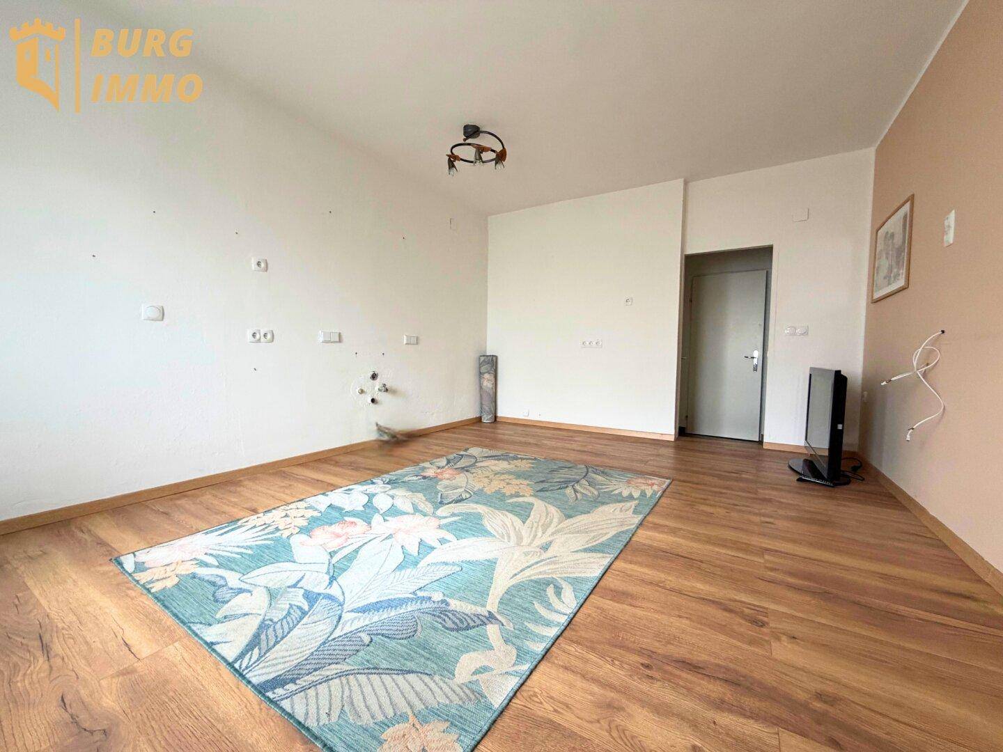 Leerer Raum mit Holzboden und einem bunten Teppich, bereit zur Einrichtung.