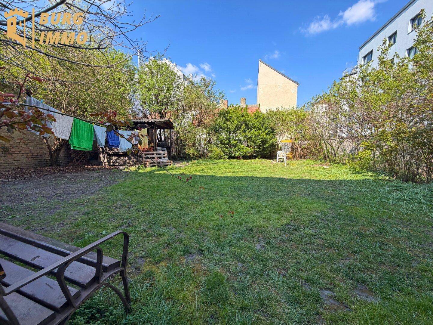 Weitläufiger Gartenbereich mit Rasenfläche, Bäumen und einem kleinen Sitzbereich im Freien.