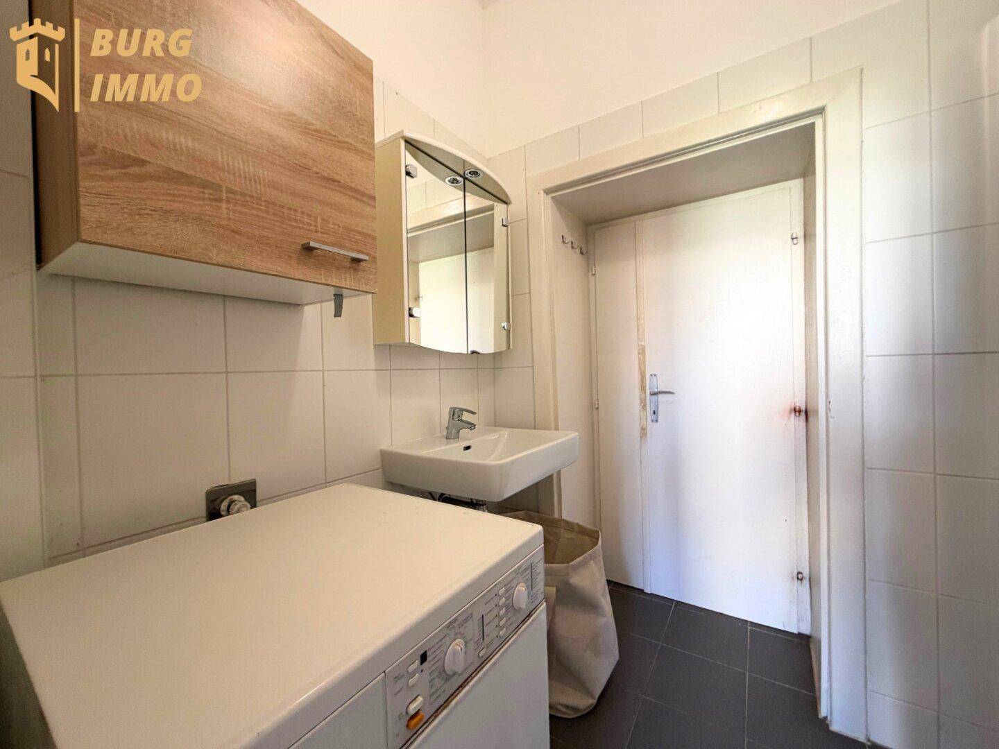Praktischer Hauswirtschaftsraum mit Waschmaschine, Waschbecken und Wandfliesen.