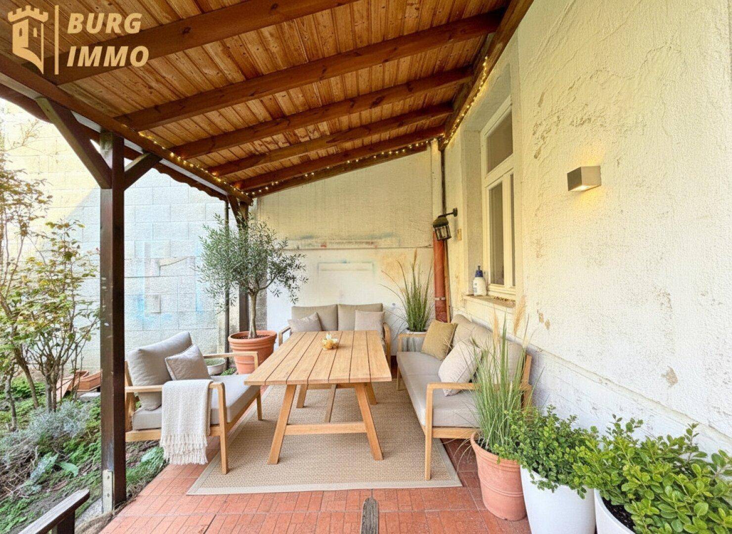 Gemütliche überdachte Terrasse mit Holzdach, bequemen Gartenmöbeln und stimmungsvoller Beleuchtung.
