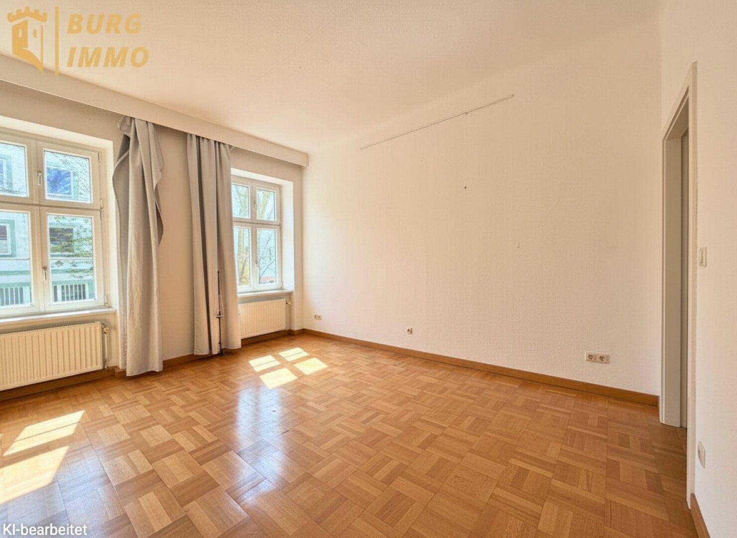 Lichtdurchflutetes Zimmer mit Parkettboden, großen Fenstern und Vorhängen.