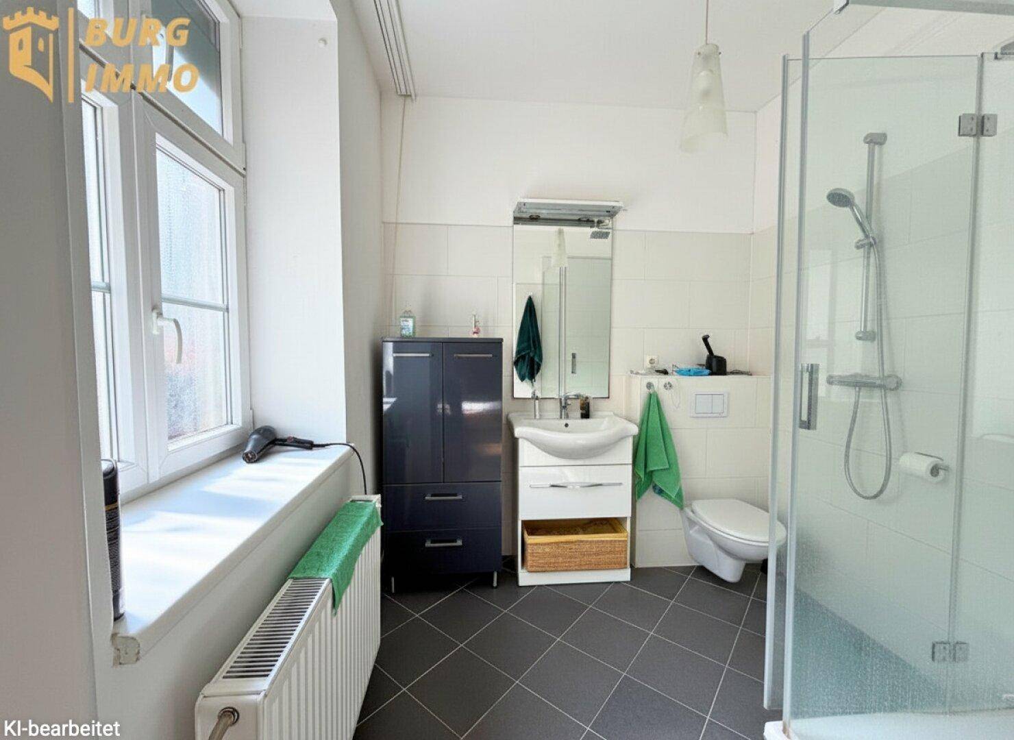 Modernes Badezimmer mit Dusche, Fenster, Waschbecken und dunklen Bodenfliesen.