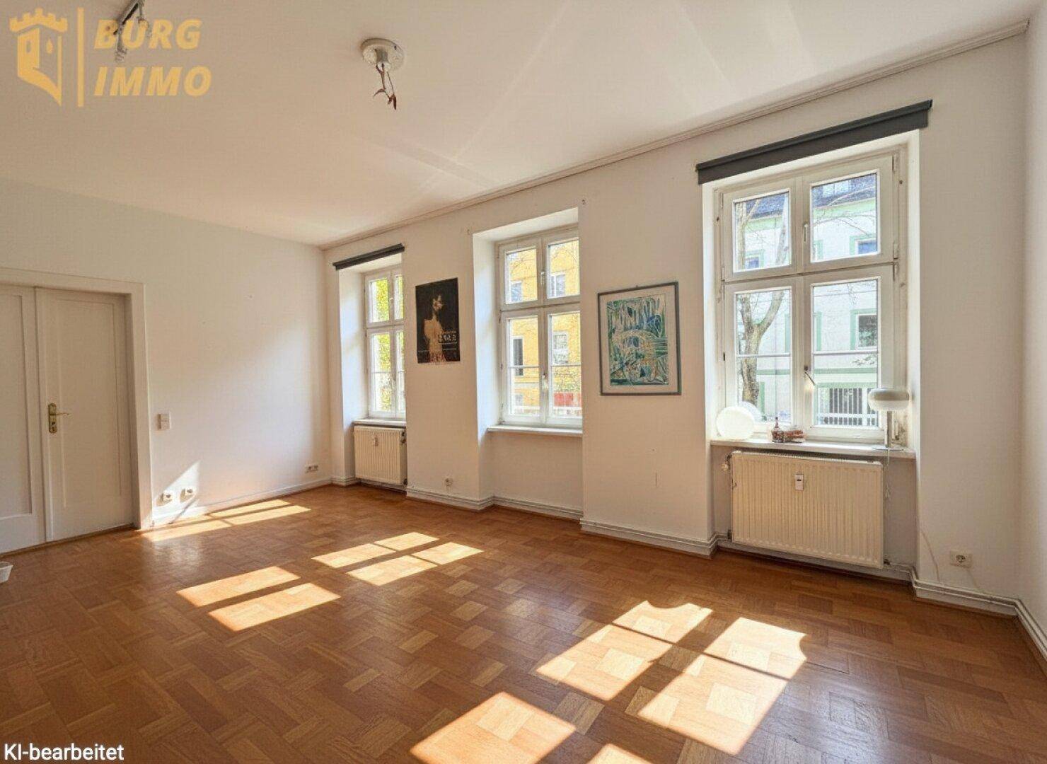 Geräumiges Wohnzimmer mit Fischgrätparkett, großen Fenstern und viel Tageslicht.