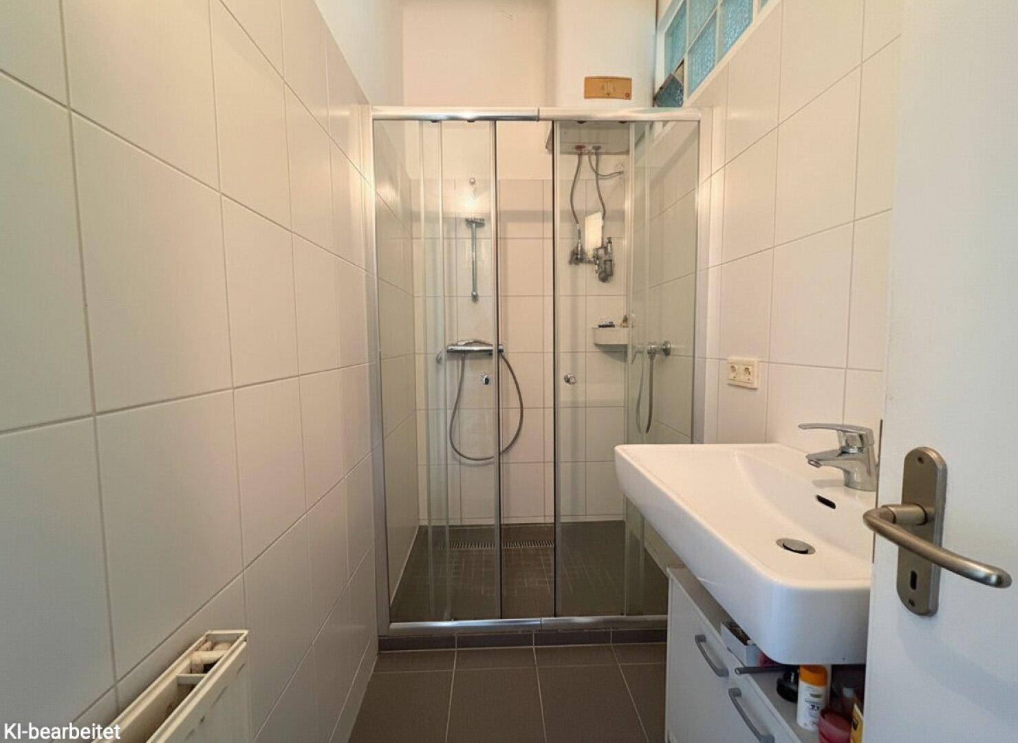 Funktionales Badezimmer mit Duschkabine, Waschbecken und weißen Wandfliesen.