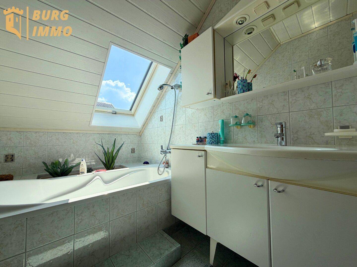 Badezimmer im Dachgeschoss mit Badewanne, Waschbecken und einem Dachfenster für Tageslicht.