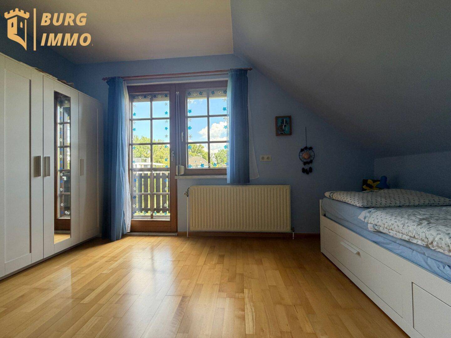 Schlafzimmer mit Holzboden, weißem Kleiderschrank und Zugang zu einem kleinen Balkon.