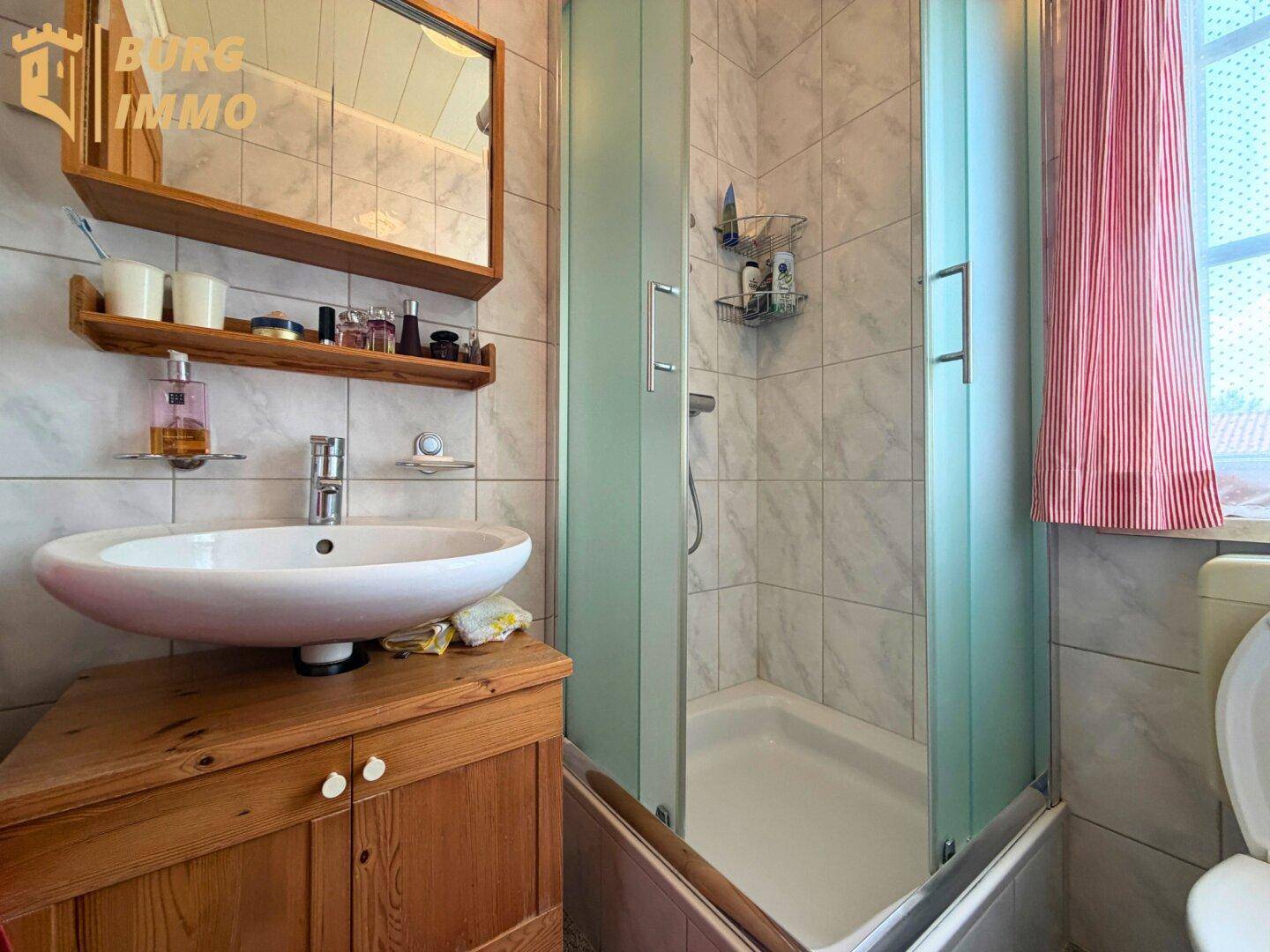 Kleines Badezimmer mit Dusche, Waschbecken auf Holzunterschrank und Wandfliesen.