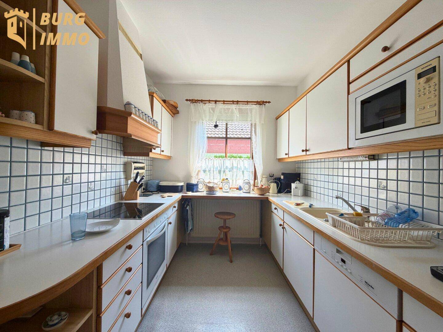 Funktionale Küche mit weißen Schränken, Holzdetails und Fliesen an den Wänden.