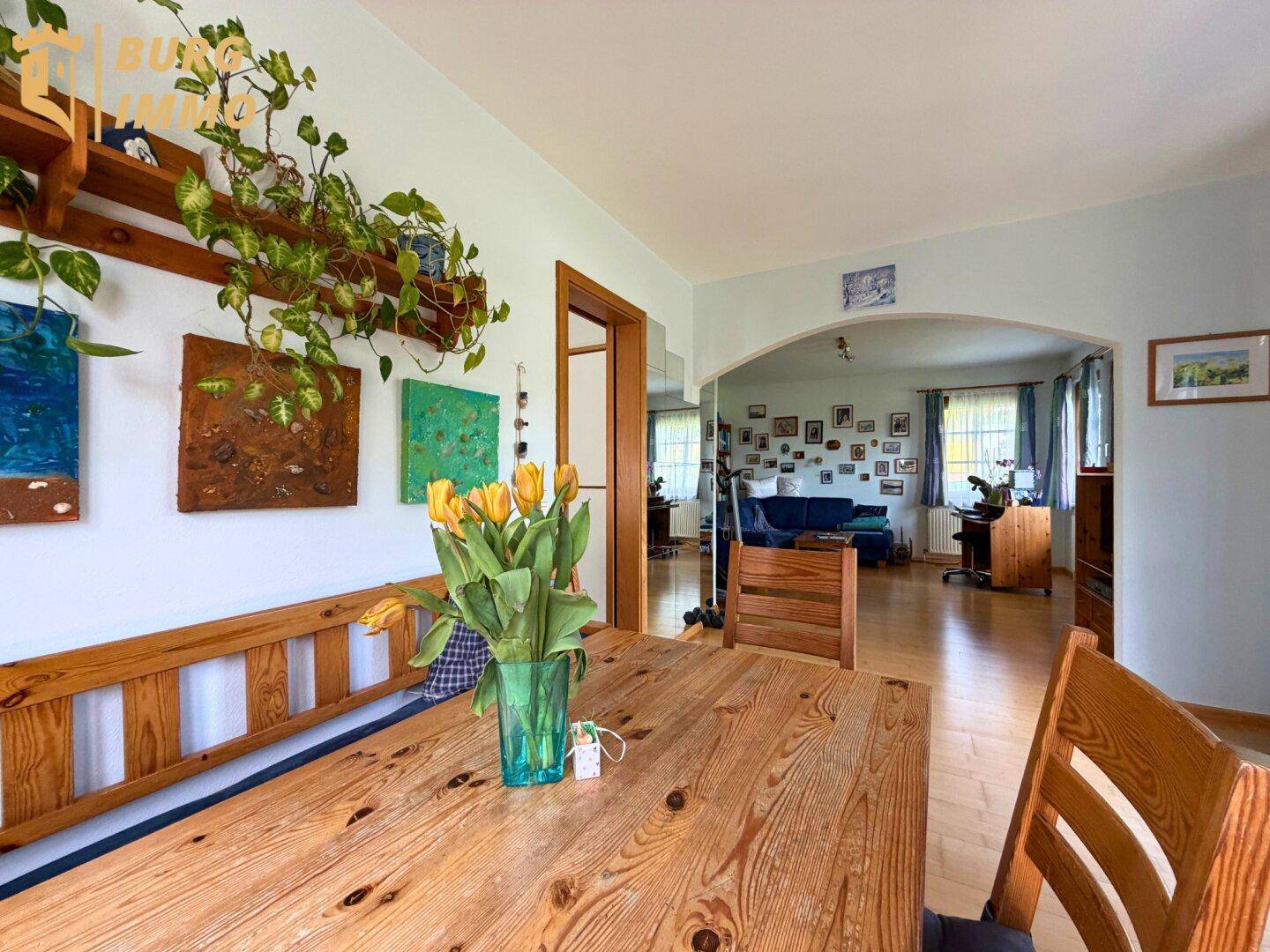 Gemütlicher Essbereich mit Holztisch und Blick in das angrenzende Wohnzimmer durch einen Rundbogen.