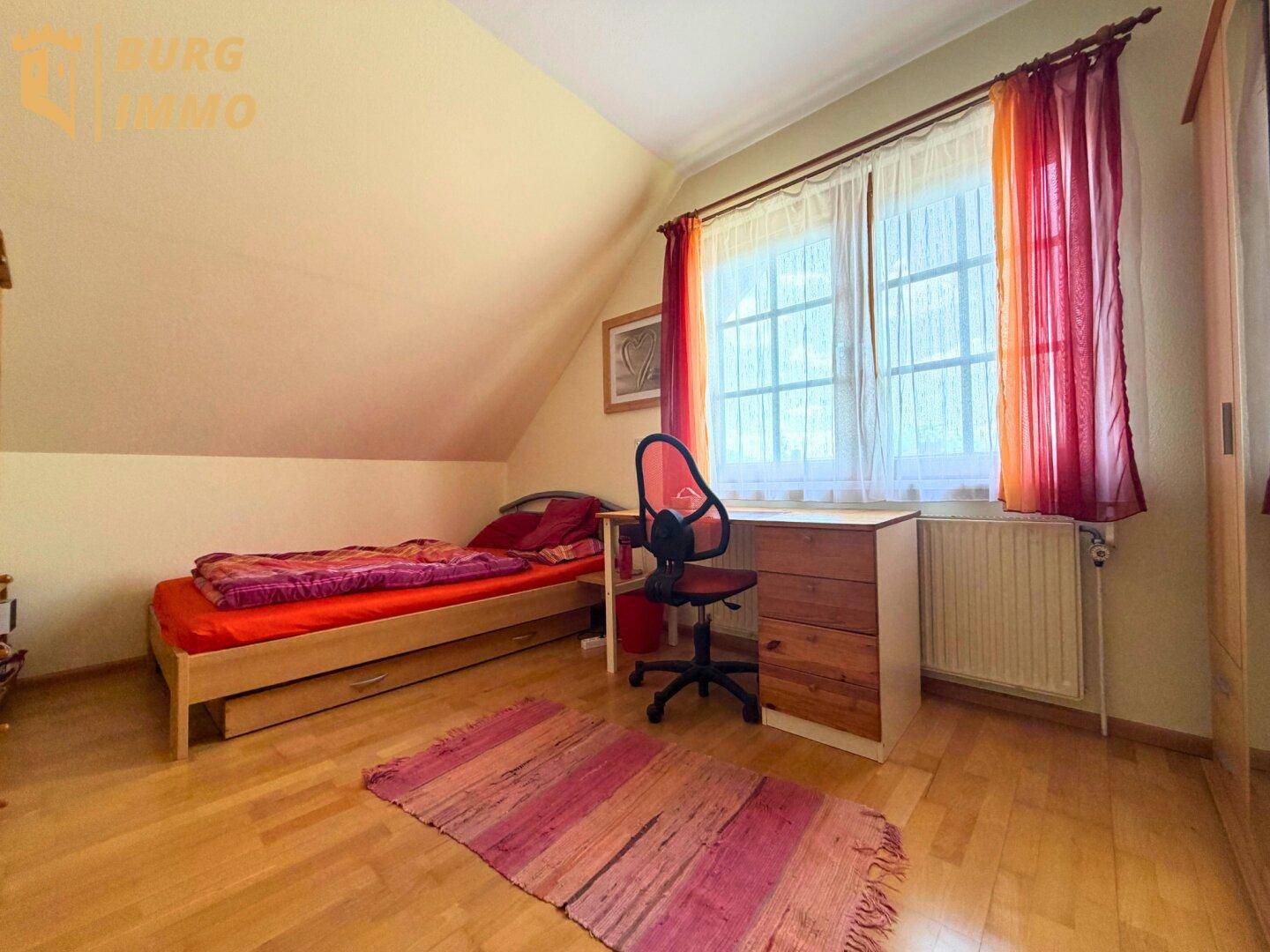 Gemütliches Schlafzimmer im Dachgeschoss mit Holzboden, Einzelbett und Schreibtisch.