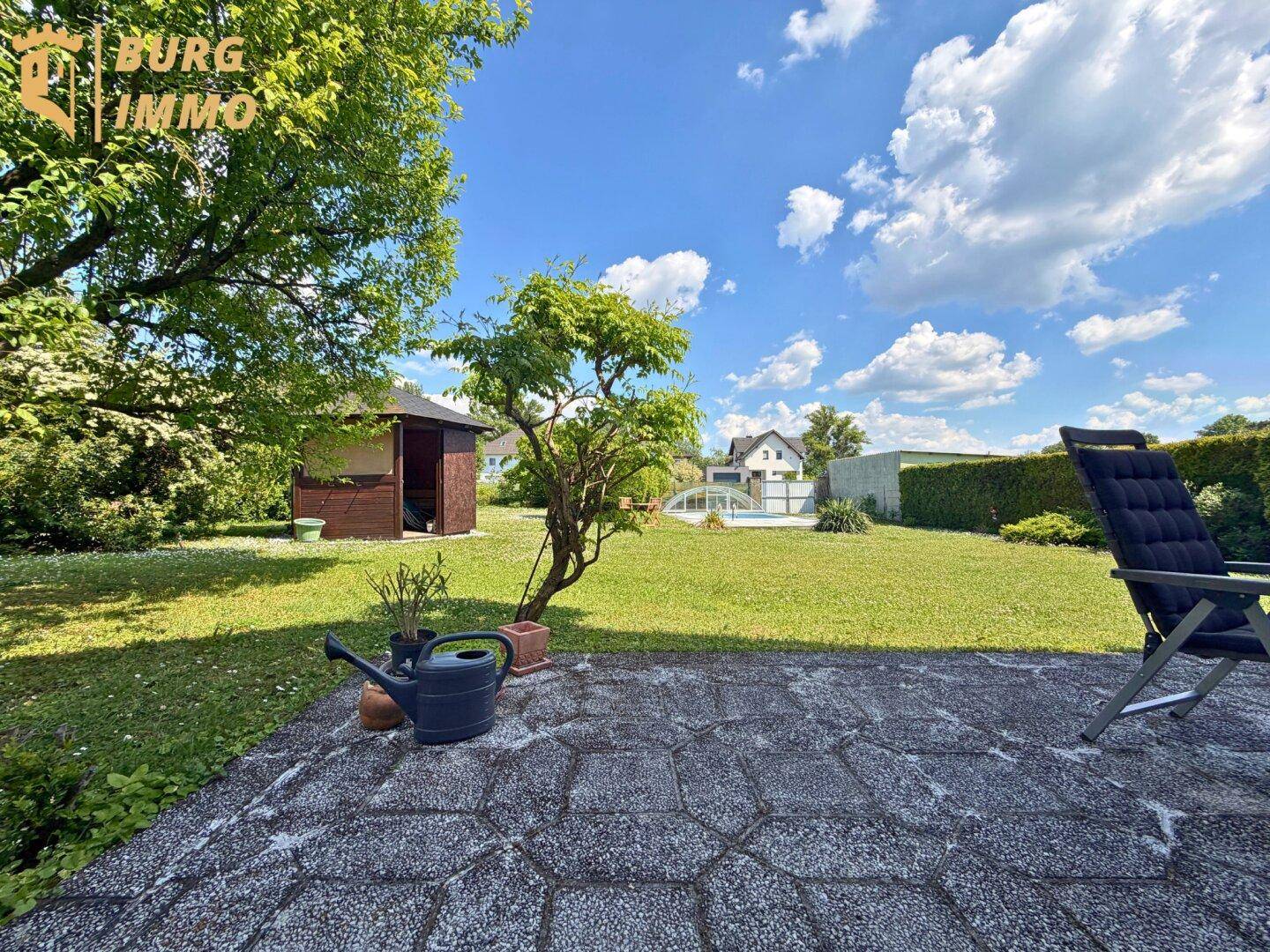 Entspannter Gartenbereich mit kleiner Terrasse, Gartenhaus und Liegestuhl im Grünen.