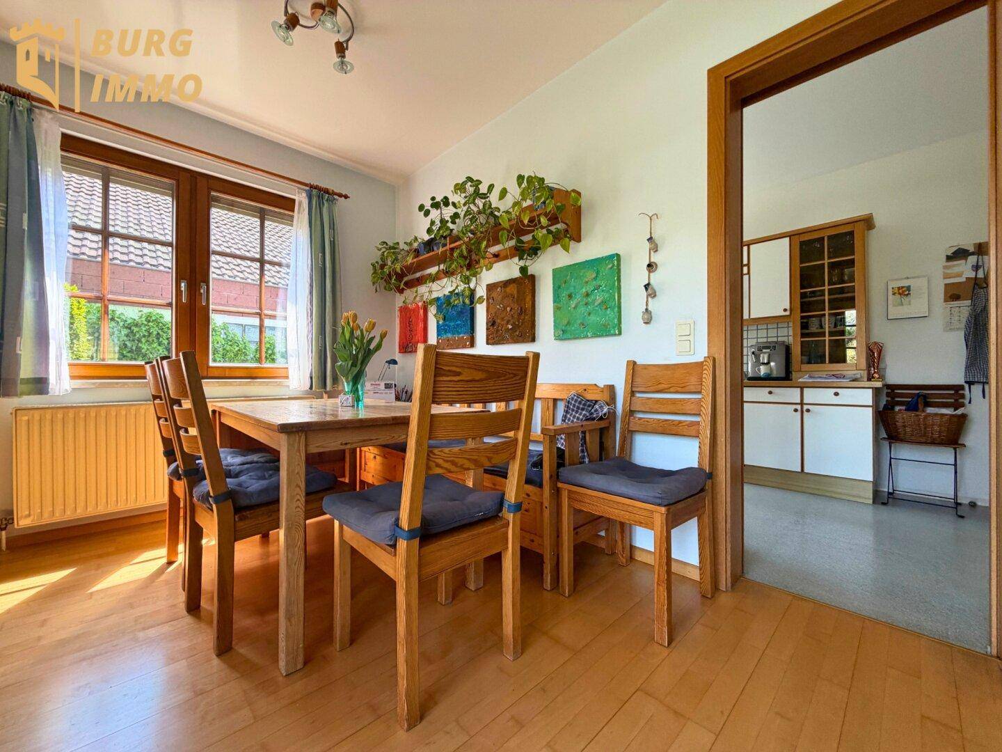 Heller Essbereich mit Holztisch und Stühlen, Fenster mit Blick ins Grüne und Zugang zur Küche.