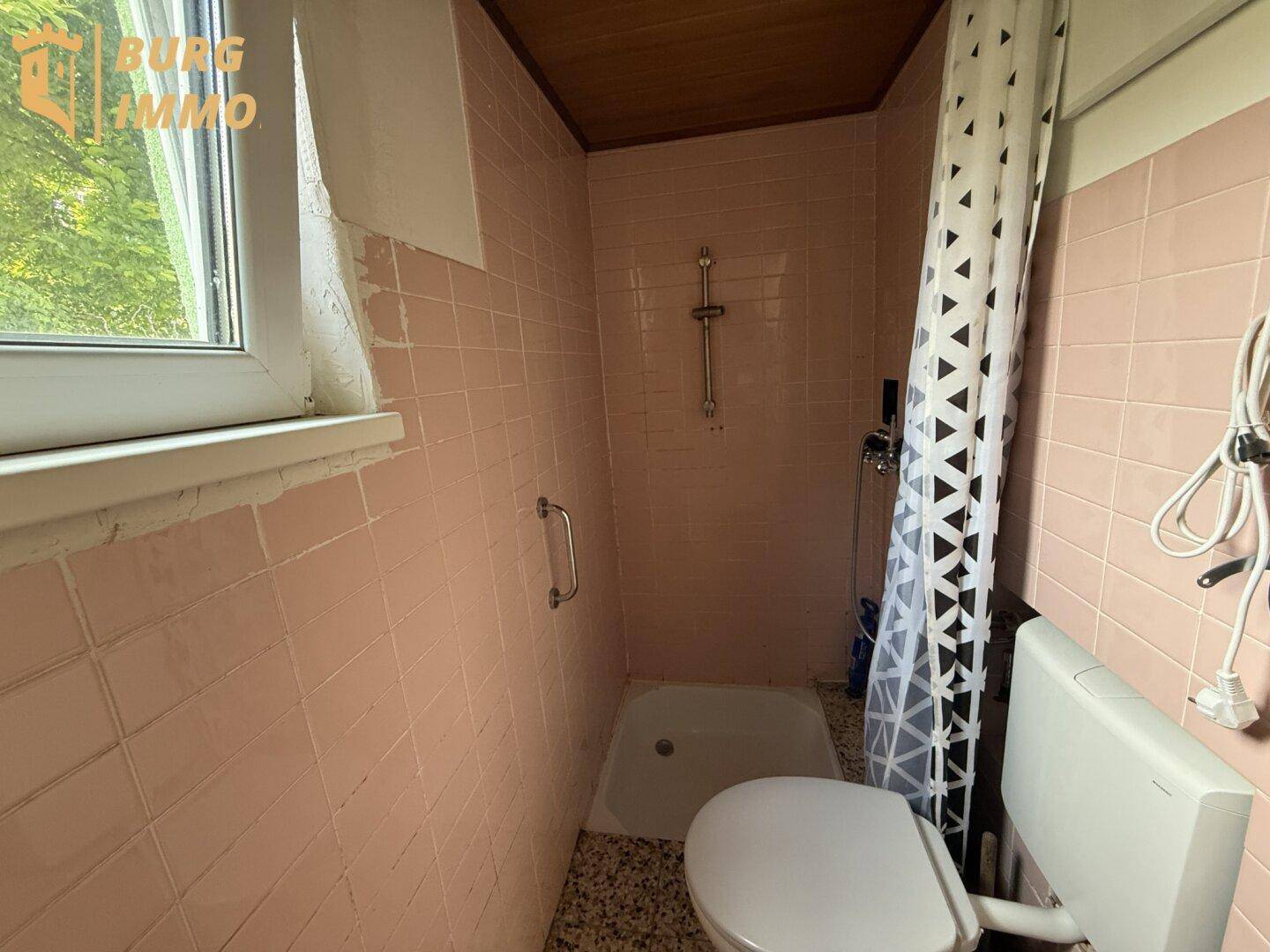 Badezimmer mit rosa Fliesen, Dusche, Toilette und einem Fenster.