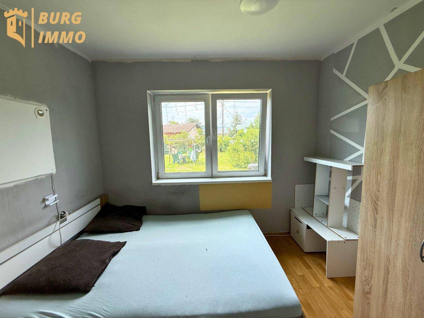 Schlafzimmer mit Holzboden, einem Bett und Blick ins Grüne durch das Fenster.