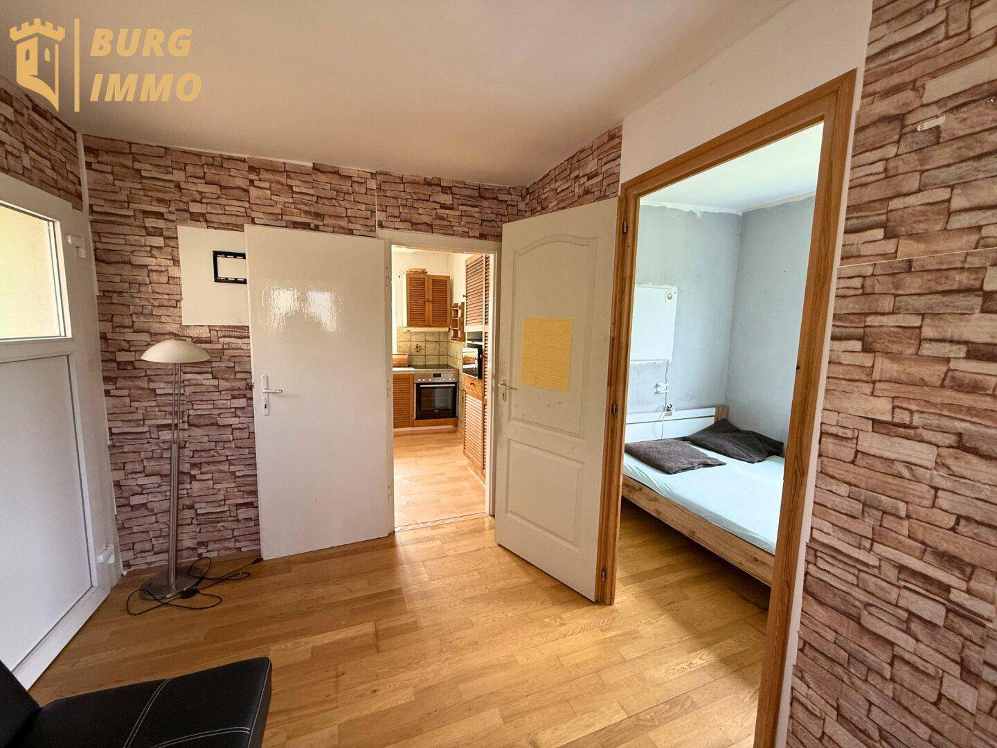 Innenraum mit Holzboden, Ziegelwandtapete und Zugängen zu Küche und Schlafzimmer.