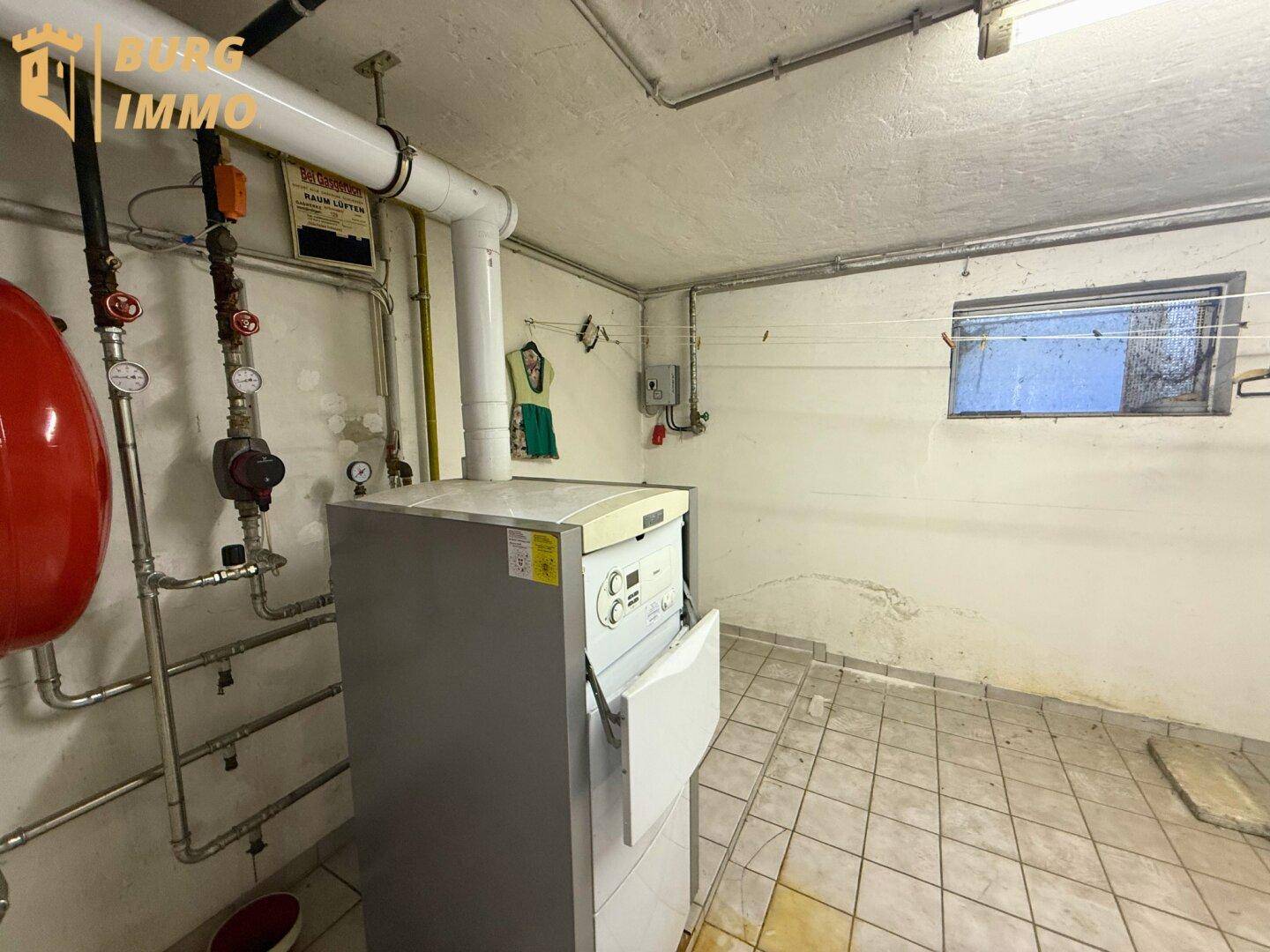 Heizungsraum im Keller mit Heizkessel, Warmwasserspeicher und Fliesenboden.