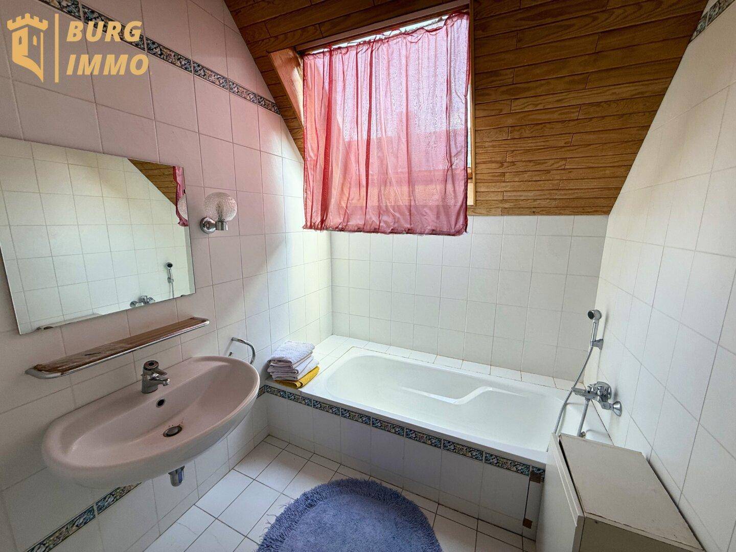 Badezimmer mit Badewanne, Waschbecken, weißen Fliesen und Dachschräge.