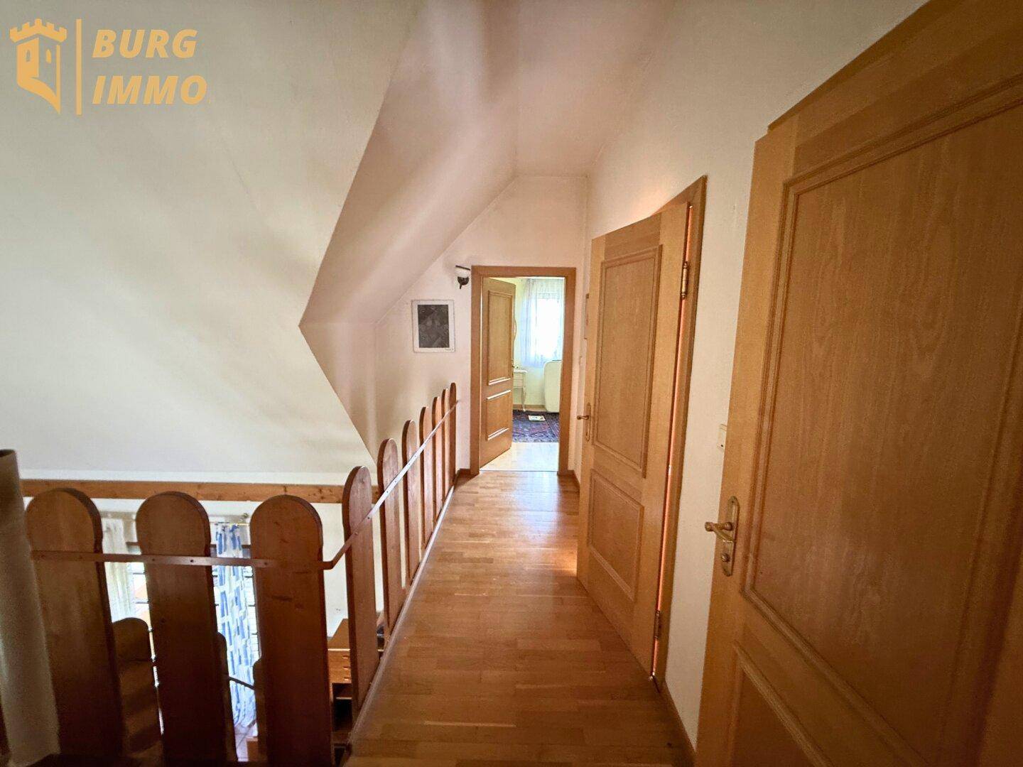 Heller Flur im Obergeschoss mit Holzgeländer und Zugang zu weiteren Zimmern.