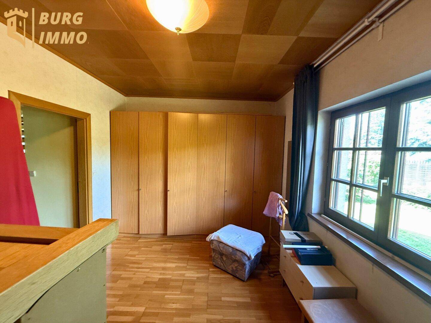 Schlafzimmer mit Einbauschränken, Holzdecke und großem Fenster mit Blick ins Grüne.