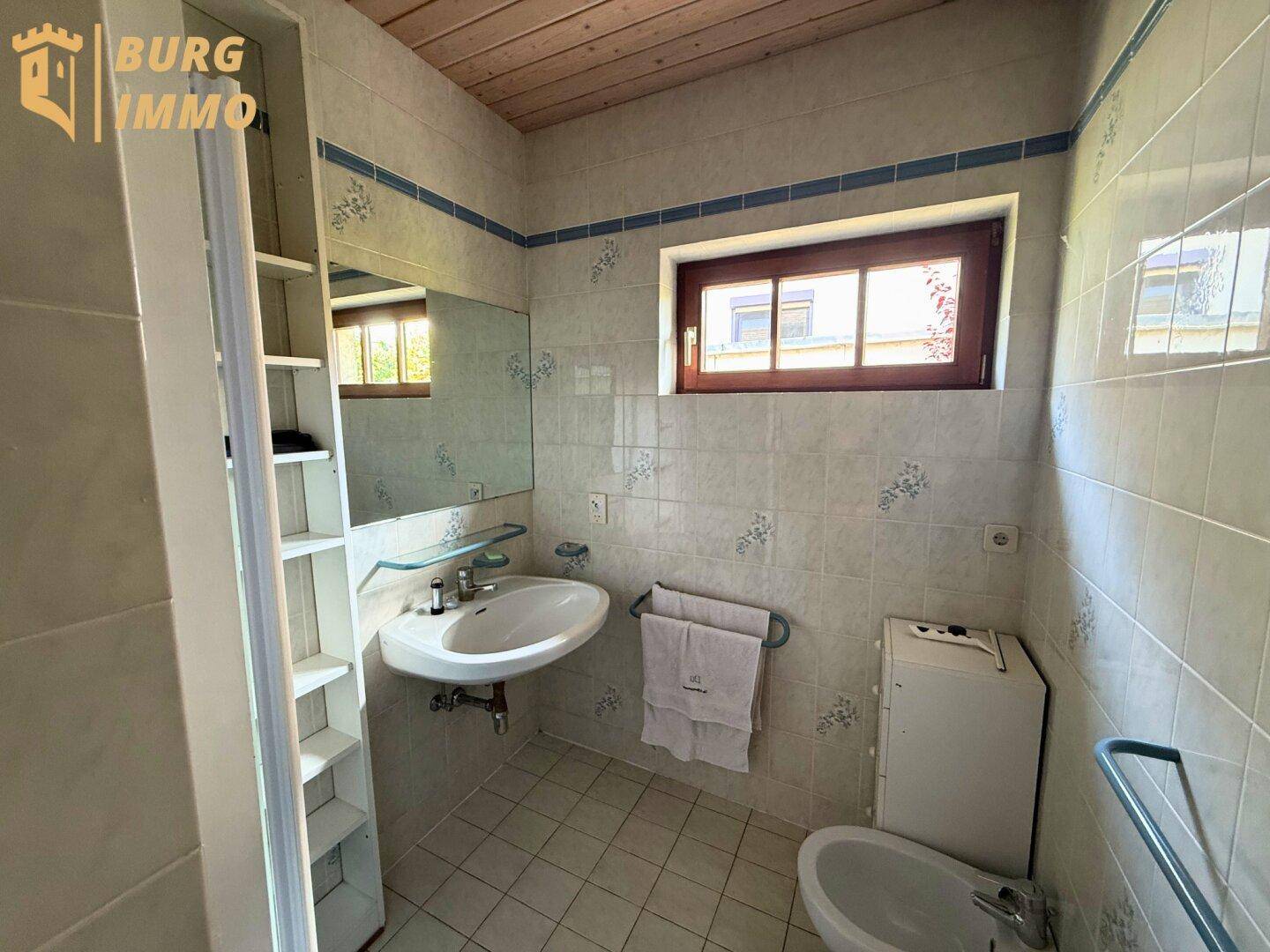 Helles Badezimmer mit Waschbecken, Bidet, Fenster und hellen Fliesen.