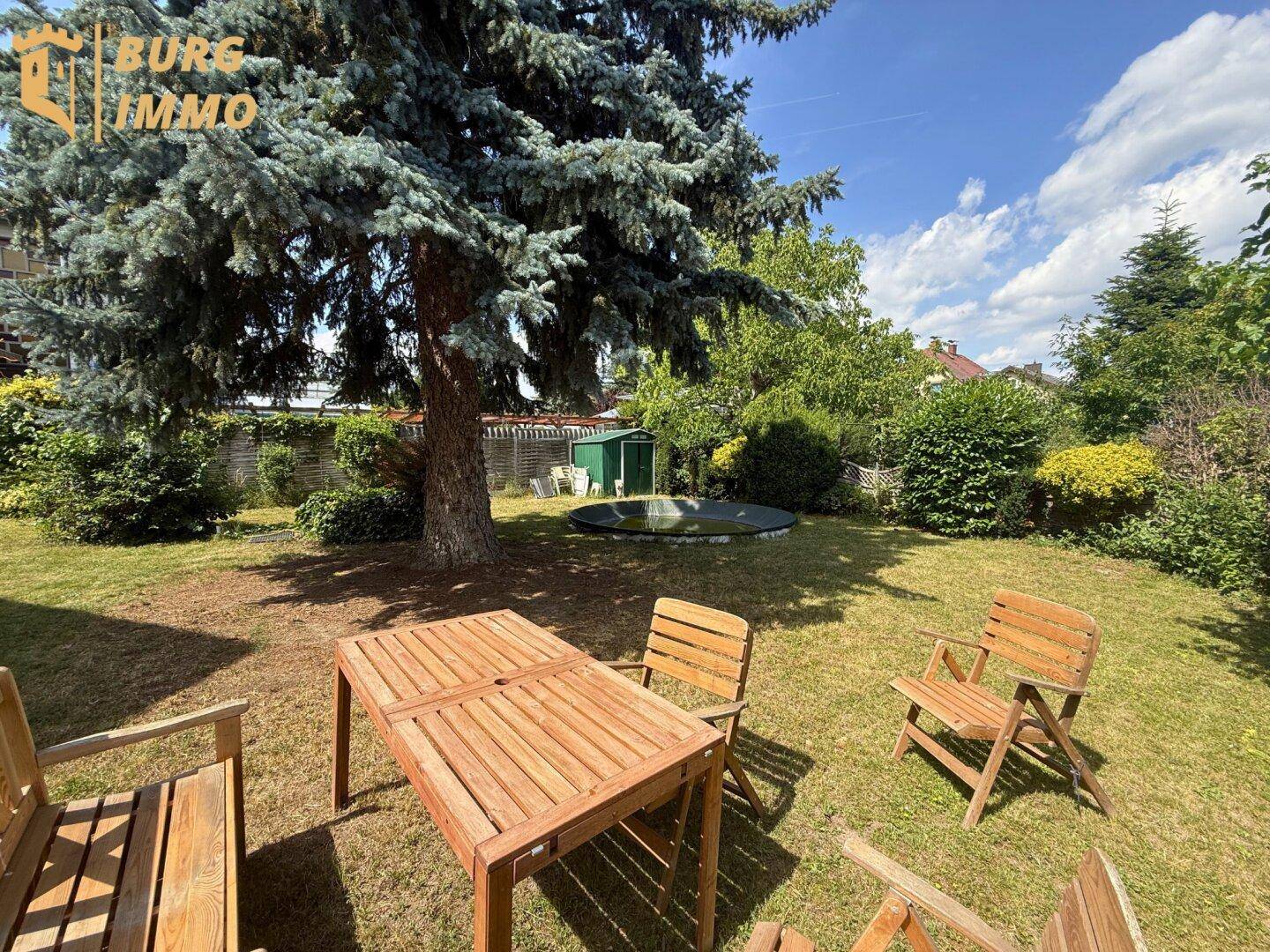 Weitläufiger Garten mit Rasenfläche, großem Baum und einem kleinen Aufstellpool.