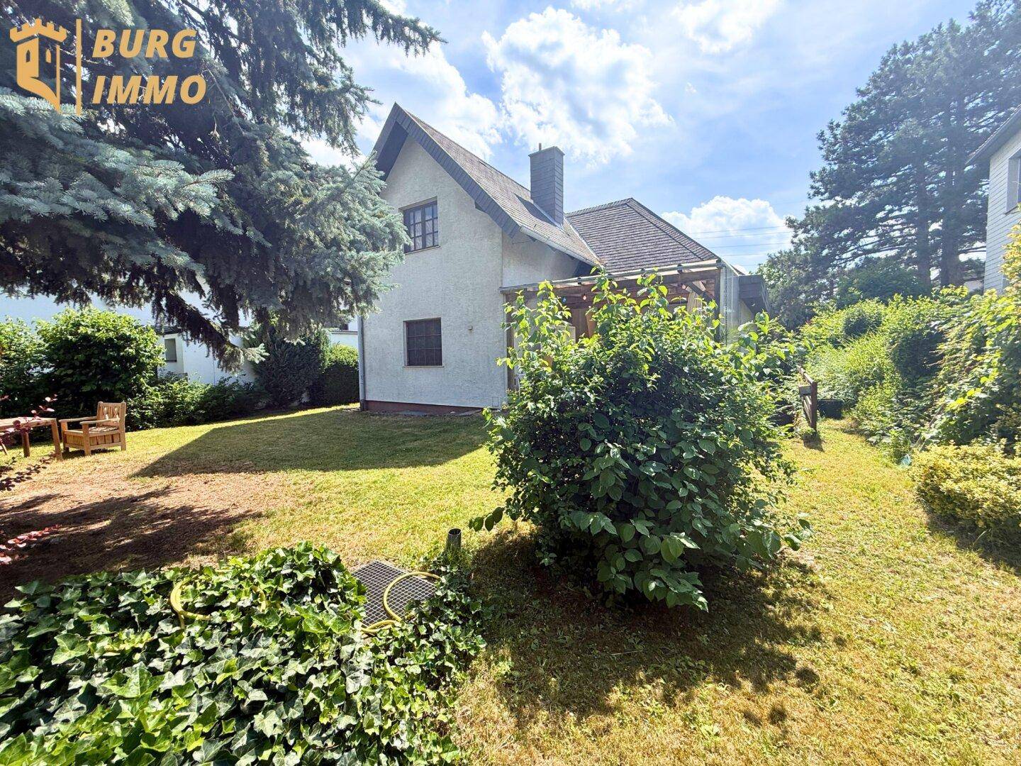 Seitlicher Blick auf das Haus mit Garten, Rasenfläche und üppiger Bepflanzung.
