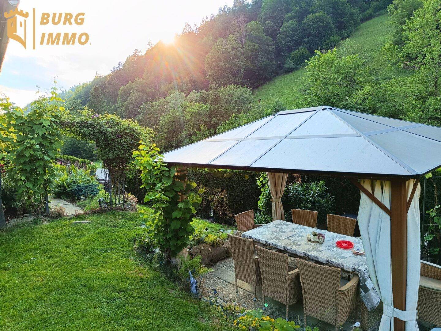 Gemütlicher Essbereich im Garten unter einem Pavillon mit Blick auf bewaldete Hügel.