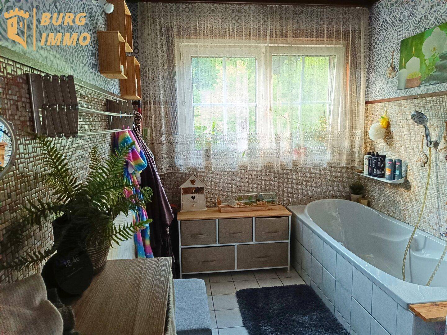 Badezimmer mit Badewanne, gemusterten Fliesen und Fenster für Tageslicht.