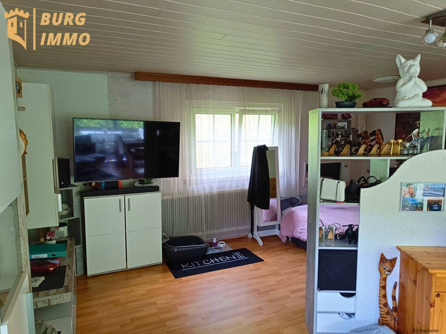 Schlafzimmer mit Fernseher, Regalen und Fenster, das viel Tageslicht hereinlässt.