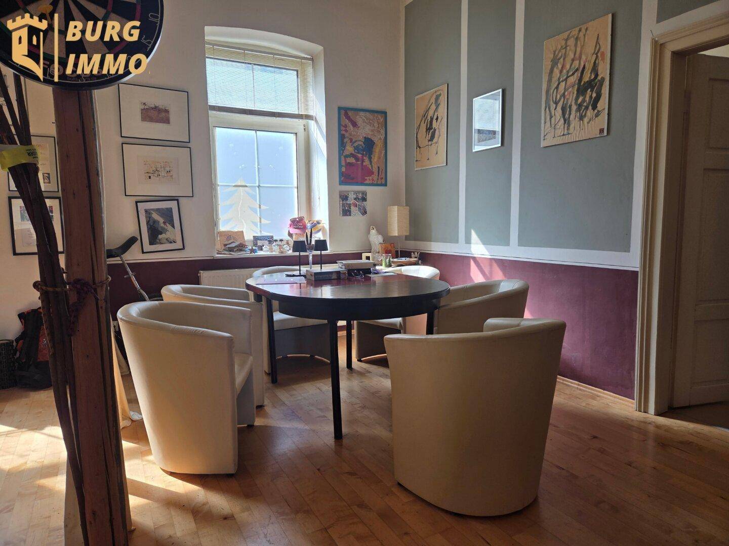 Essbereich mit rundem Tisch, vier Stühlen, Holzdielenboden und Kunstwerken an den Wänden.