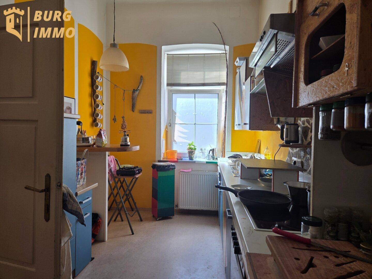 Küche mit gelben Wänden, kleinem Fenster, einfachen Schränken und einer Frühstücksbar.