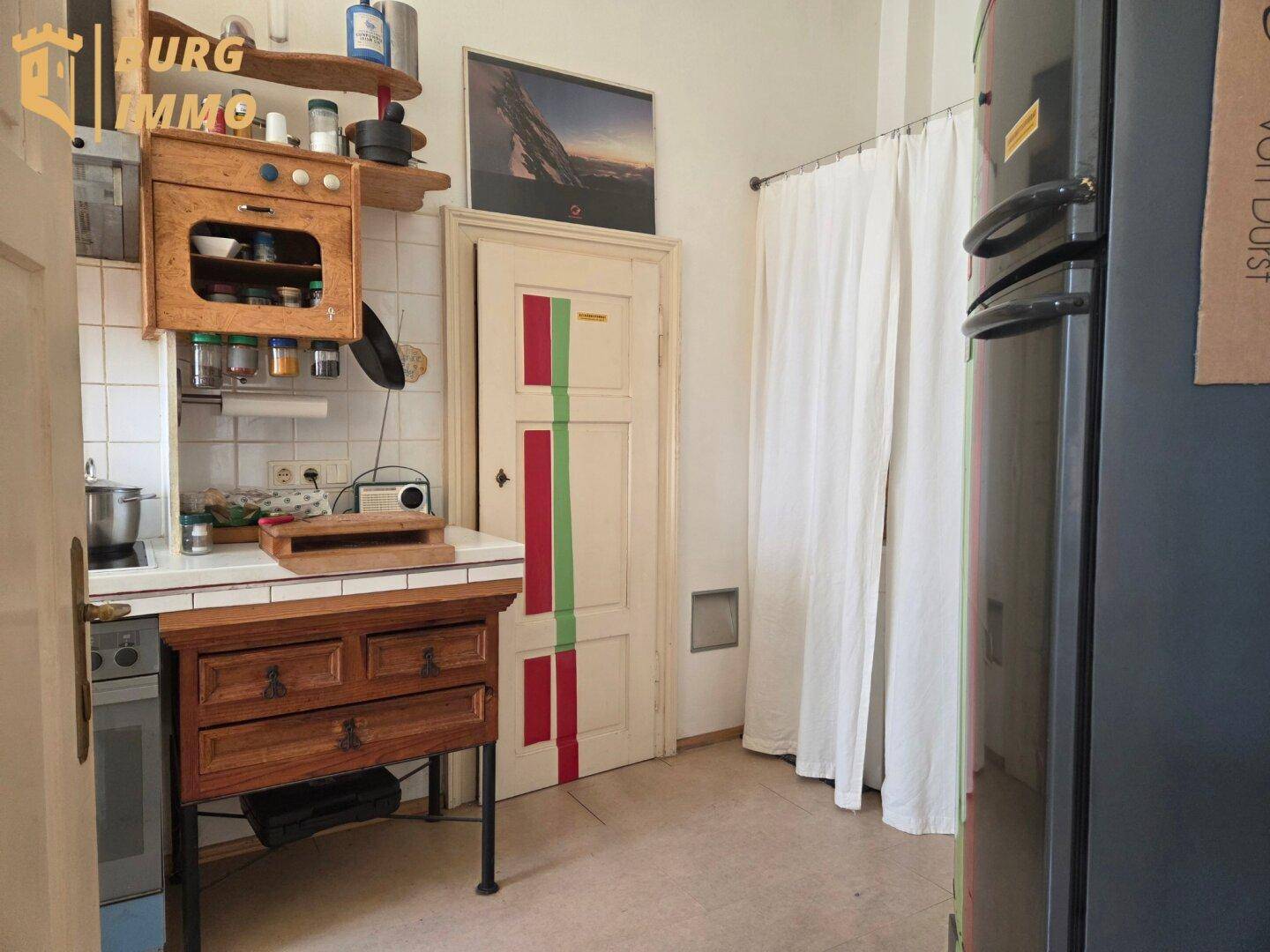 Rustikale Küche mit Kühlschrank, einfachen Holzschränken und einer Tür mit farbigen Streifen.
