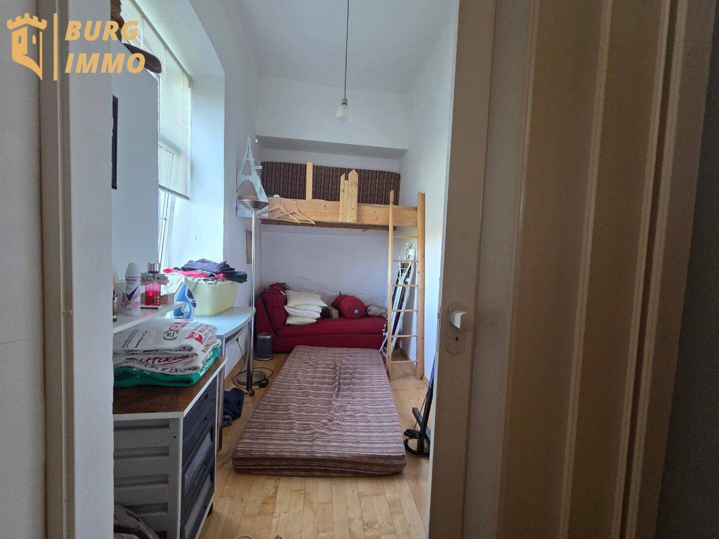 Kleines Zimmer mit Etagenbett, Sofa und Matratze auf dem Boden, ideal als Kinder- oder Gästezimmer.